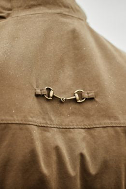 Bronze-tone horse bit clasp detail on back yoke of brown Ariat Argentium Parka jacket