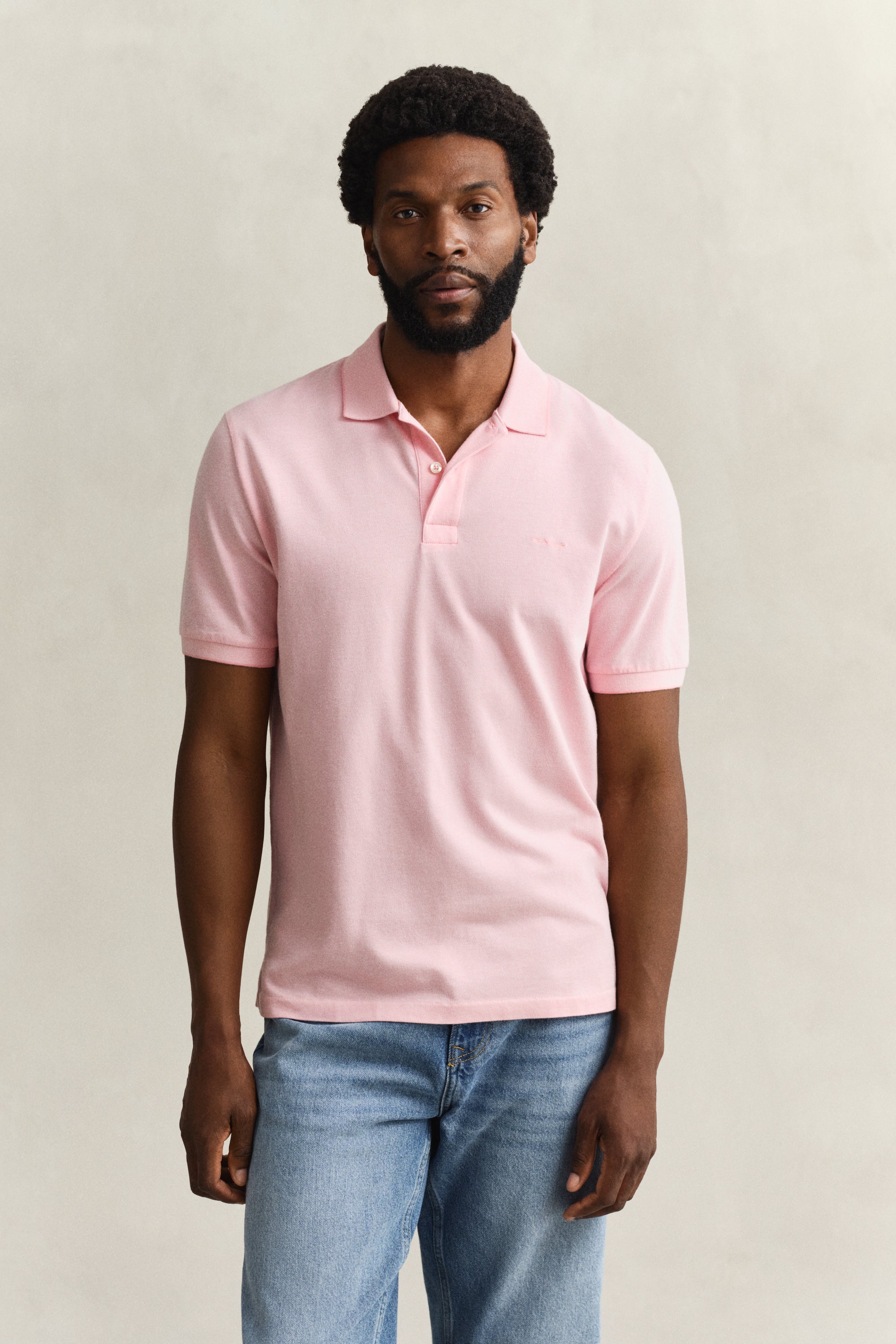 Man wearing GANT 2 Tone SS Polo in light pink with collar and two-button placket, paired with light blue jeans